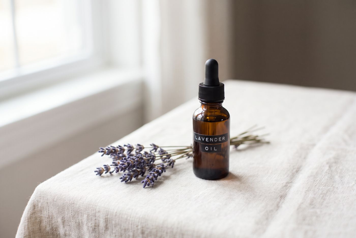 An amber bottle labelled Lavender Oil with a sprig of fresh lavender on linen